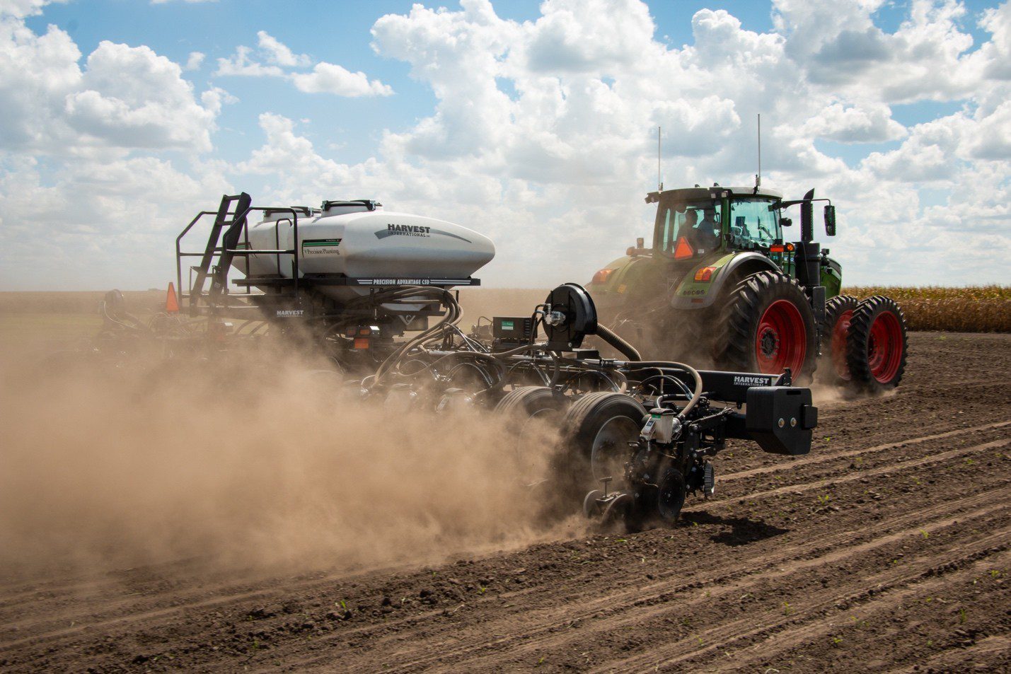 Picture13 Tractor pulling a precision planter across a dusty field under a partly cloudy sky, showing Agriteer-style precision farming equipment used for planting and data-driven crop management